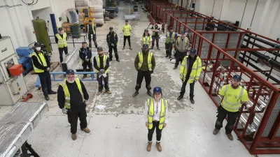 Construction workers in high vis jackets stand in a manufacturing facility
