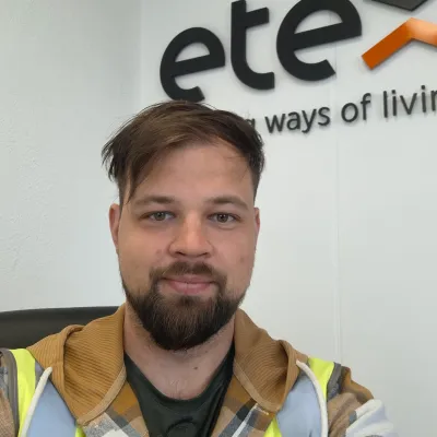 A person wearing a high-visibility vest and a hoodie, smiling in front of a white wall with the logo "etex" visible in the background.